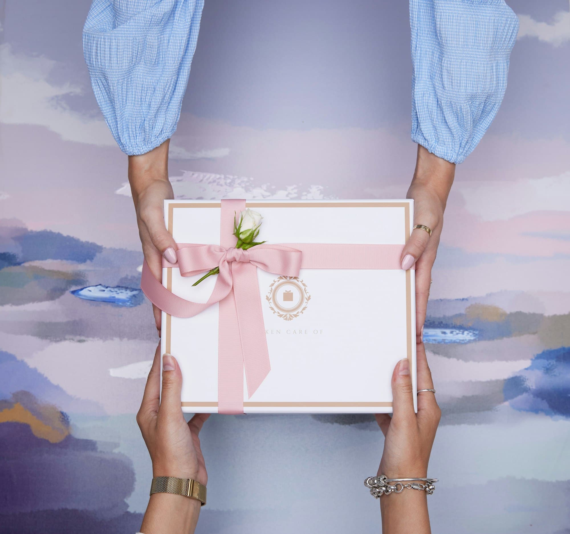 Two hands passing a white gift box tied with a pink ribbon